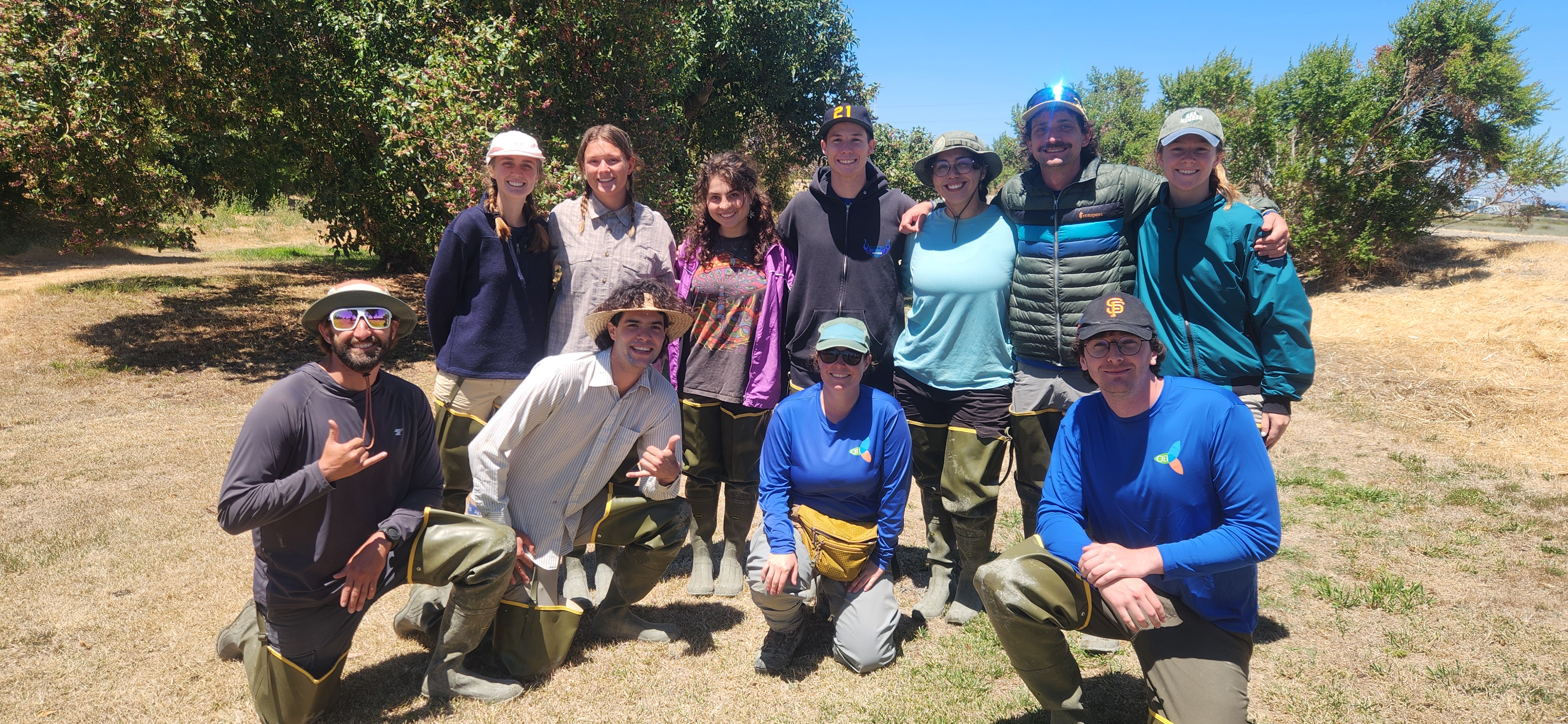 A group of young people in hiking clothes and outdoor gear smile in a sunny field